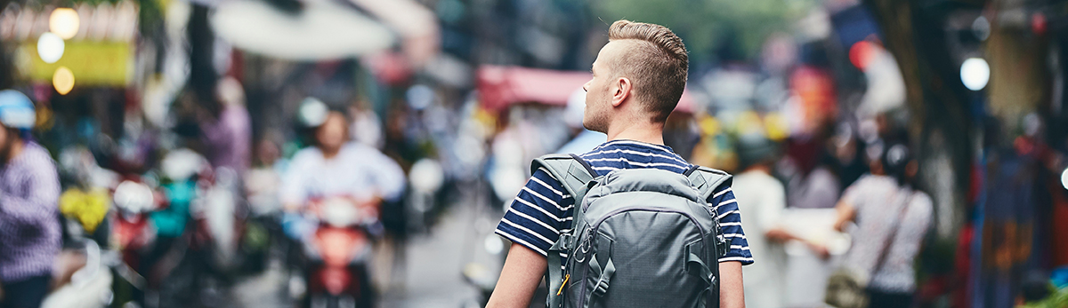 young man with backpack walks through a city street in Asia